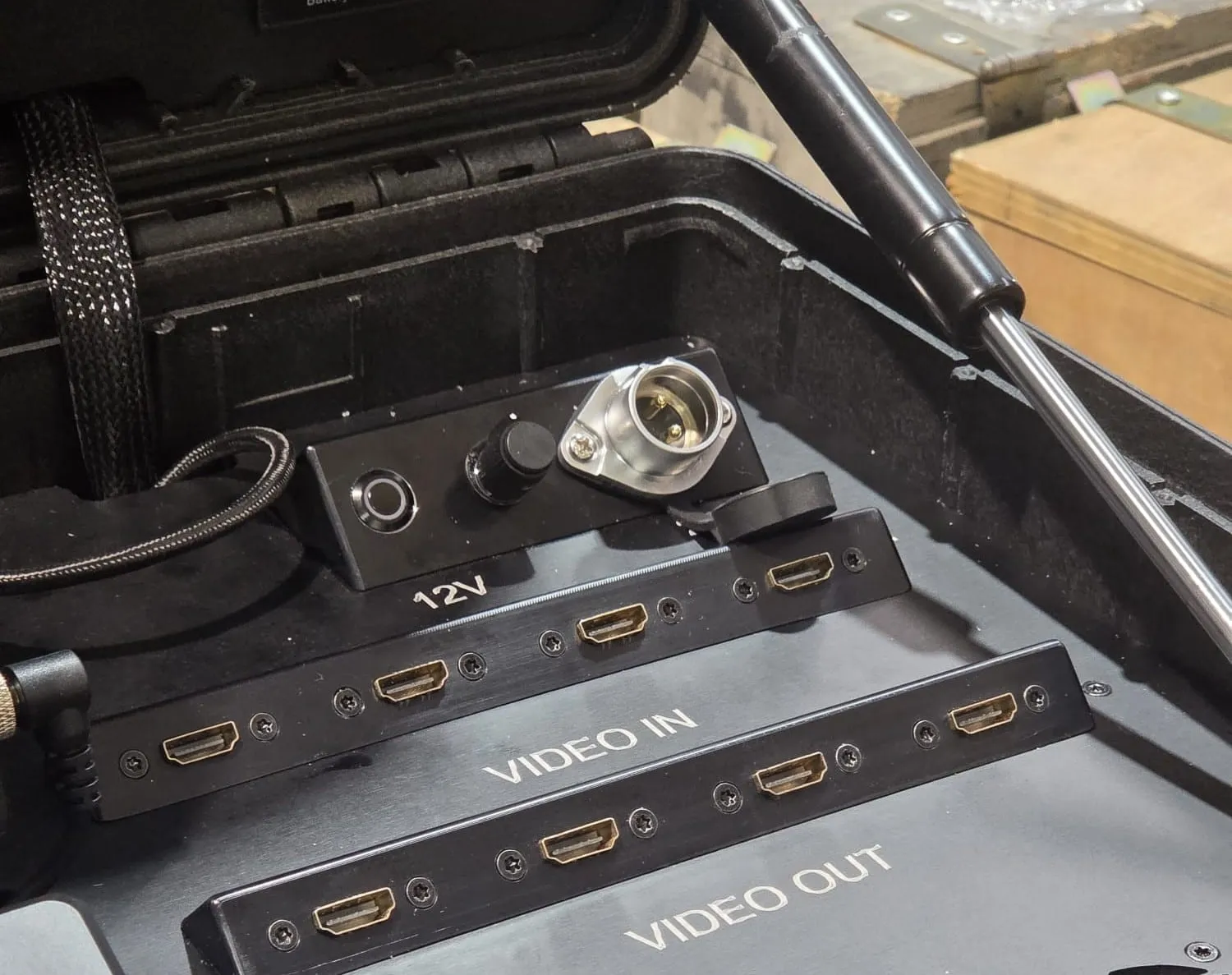 לוח הממשקים בתוך המארז הפתוח: כניסת מתח 12V עם מפסק ומחבר נעילה קשיח, מעל לוחות VIDEO IN ו-VIDEO OUT ובהם ארבע יציאות HDMI כל אחד, מכוסות בפקקי גומי